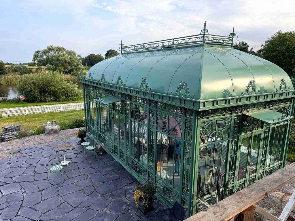 Green Victorian greenhouse with plain roof beside water in Sweden.